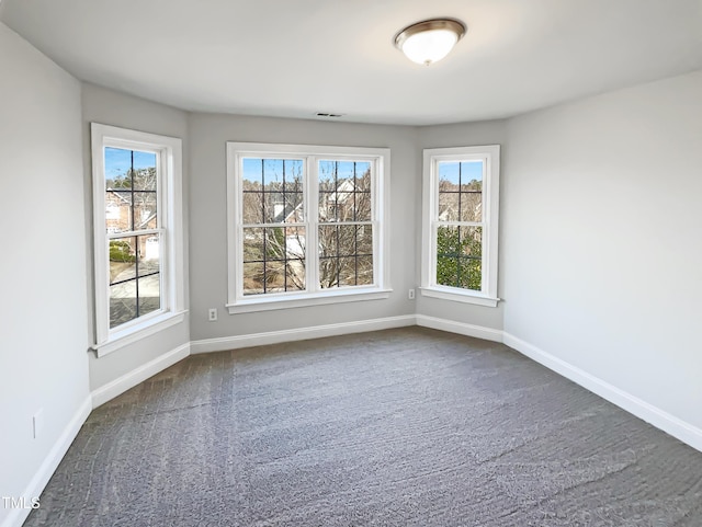 spare room with dark colored carpet, baseboards, and a wealth of natural light