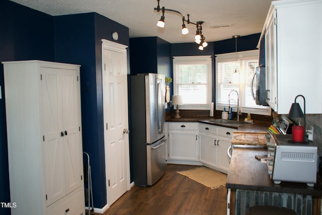 kitchen with dark wood-style floors, a sink, appliances with stainless steel finishes, white cabinetry, and dark countertops