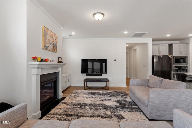 living area featuring a glass covered fireplace, wood finished floors, visible vents, and ornamental molding