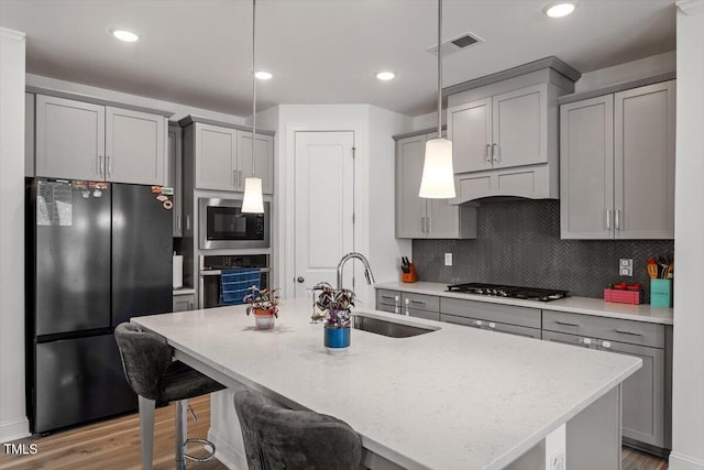 kitchen featuring visible vents, black appliances, pendant lighting, gray cabinets, and a sink