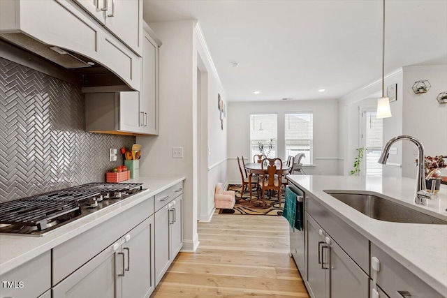 kitchen featuring decorative light fixtures, under cabinet range hood, light wood-style floors, stainless steel appliances, and a sink