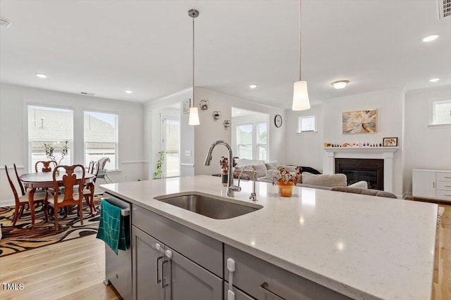 kitchen featuring a sink, gray cabinetry, light wood-style floors, a glass covered fireplace, and stainless steel dishwasher