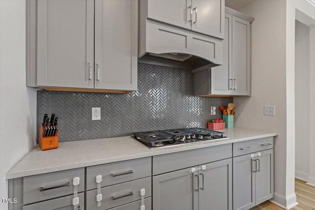 kitchen featuring under cabinet range hood, decorative backsplash, gray cabinetry, and stainless steel gas cooktop