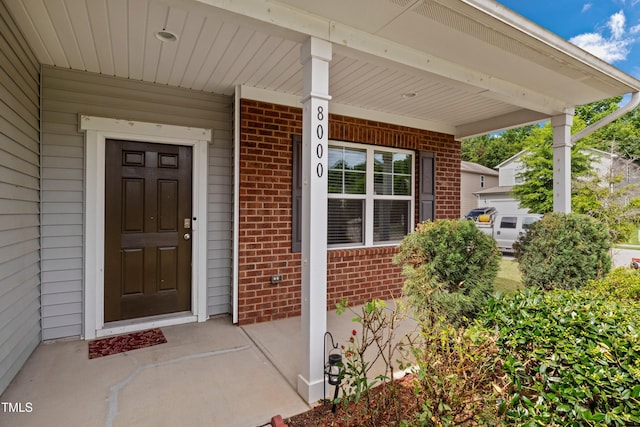 doorway to property featuring a porch and brick siding