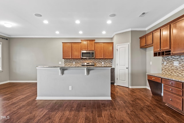 kitchen with light stone counters, visible vents, built in desk, appliances with stainless steel finishes, and brown cabinets