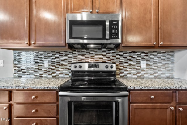 kitchen with stainless steel appliances, light stone countertops, tasteful backsplash, and brown cabinets