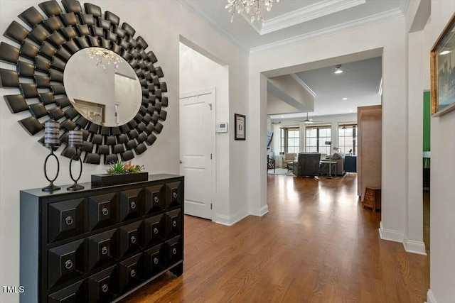 corridor with an inviting chandelier, wood finished floors, baseboards, and ornamental molding