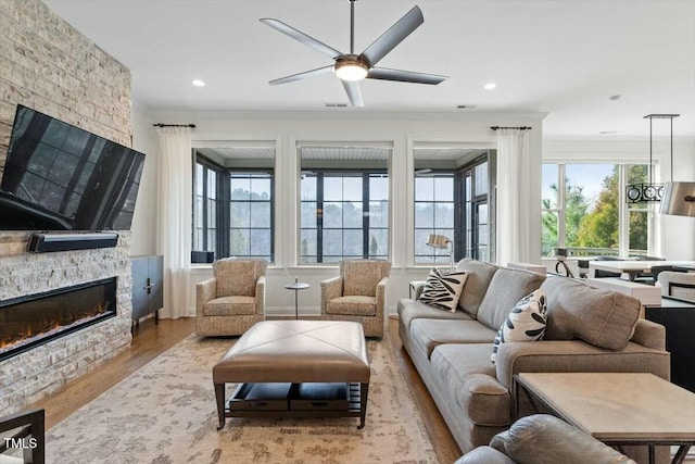 living room with a ceiling fan, wood finished floors, visible vents, a fireplace, and ornamental molding