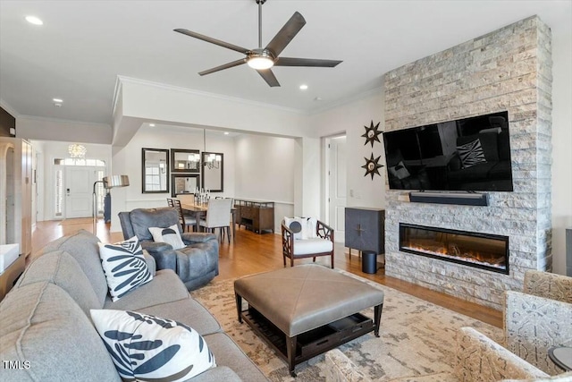 living area with ornamental molding, a stone fireplace, recessed lighting, ceiling fan with notable chandelier, and wood finished floors