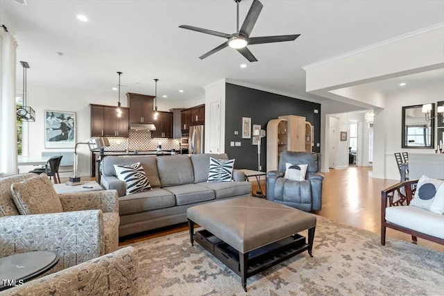 living area featuring recessed lighting, ceiling fan with notable chandelier, ornamental molding, and light wood finished floors