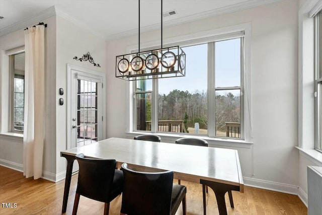 dining room featuring baseboards, visible vents, light wood-style floors, crown molding, and a notable chandelier