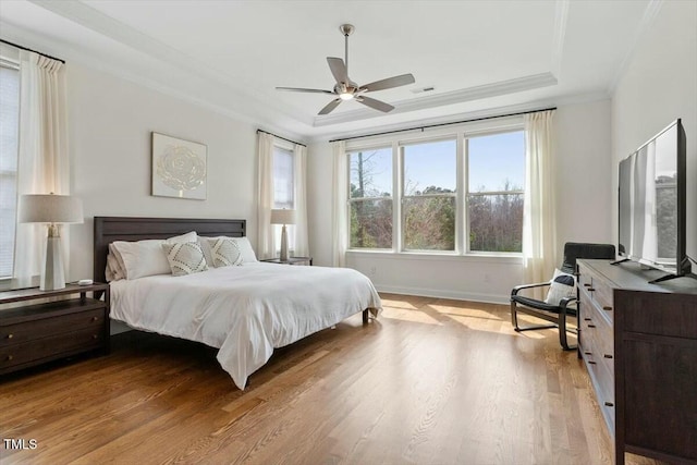 bedroom with a tray ceiling, baseboards, light wood finished floors, and ornamental molding