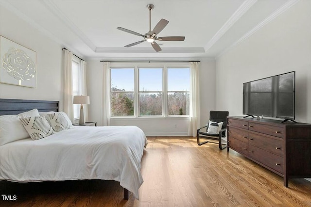 bedroom featuring a raised ceiling, ornamental molding, light wood-style floors, baseboards, and ceiling fan