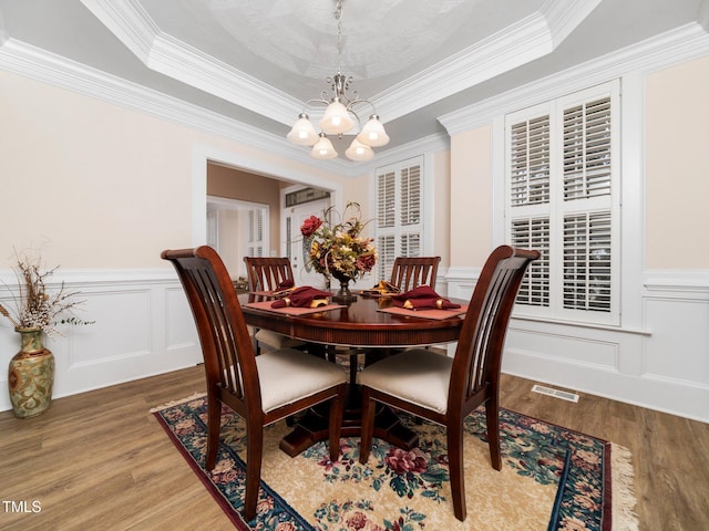 dining area featuring a decorative wall, an inviting chandelier, a tray ceiling, and wood finished floors