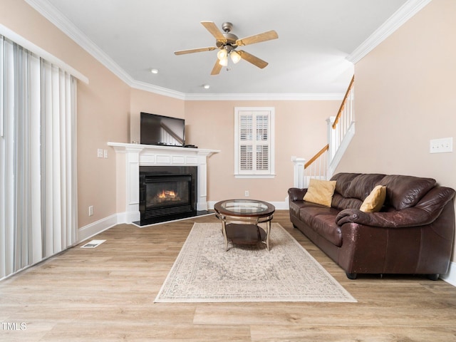 living room featuring stairway, wood finished floors, baseboards, ornamental molding, and a glass covered fireplace