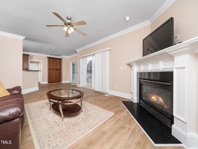 living room with a glass covered fireplace, light wood-type flooring, baseboards, and ornamental molding