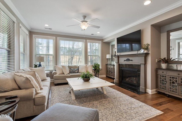 living room featuring a high end fireplace, crown molding, baseboards, wood finished floors, and a ceiling fan