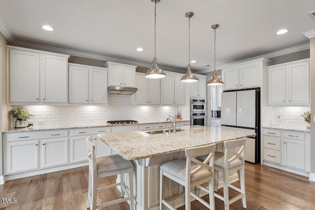 kitchen featuring under cabinet range hood, freestanding refrigerator, wood finished floors, gas stovetop, and a sink