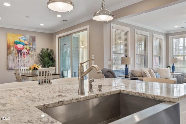 kitchen featuring pendant lighting, ornamental molding, light stone counters, recessed lighting, and a sink