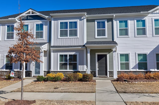 townhome / multi-family property with board and batten siding, stone siding, and a shingled roof