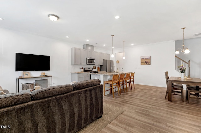 living room featuring a chandelier, baseboards, light wood-style flooring, and crown molding