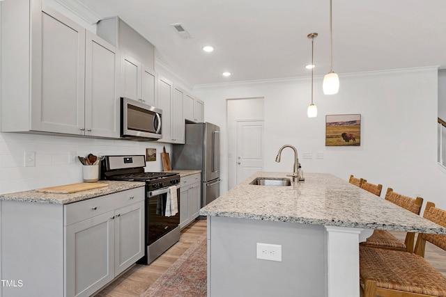 kitchen with a kitchen bar, a sink, tasteful backsplash, stainless steel appliances, and light wood finished floors