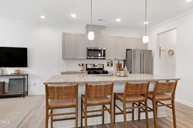 kitchen with ornamental molding, a sink, light stone counters, stainless steel appliances, and light wood finished floors