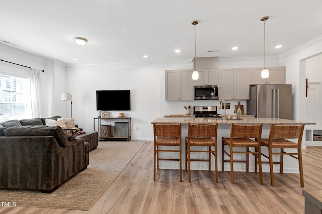 kitchen with an island with sink, ornamental molding, light wood-style floors, appliances with stainless steel finishes, and a kitchen bar