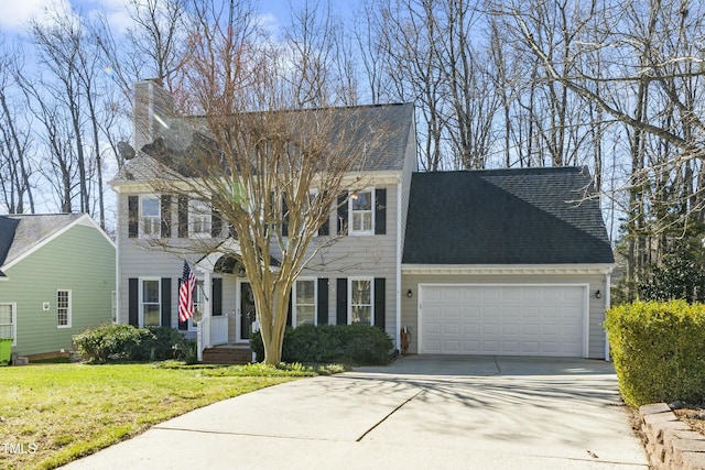 colonial-style house featuring a front yard, driveway, an attached garage, a chimney, and a shingled roof