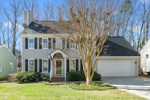 colonial house featuring a shingled roof, a front yard, a chimney, a garage, and driveway