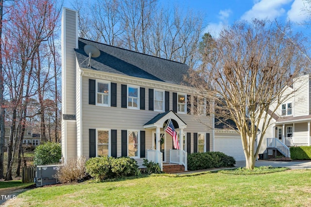 colonial house featuring a front yard, roof with shingles, driveway, a chimney, and a garage