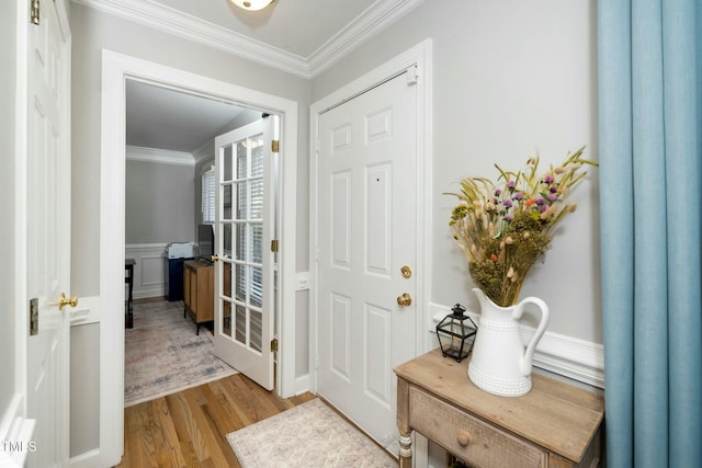 foyer featuring light wood-type flooring, wainscoting, crown molding, and a decorative wall