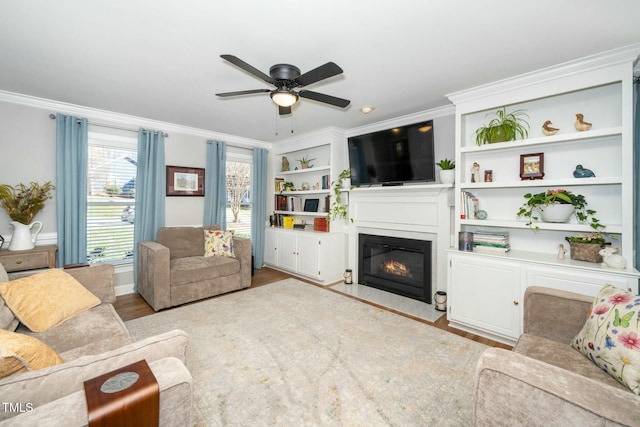 living area featuring a ceiling fan, a fireplace with flush hearth, wood finished floors, and ornamental molding