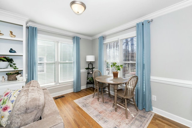 dining area with baseboards, visible vents, light wood finished floors, and ornamental molding