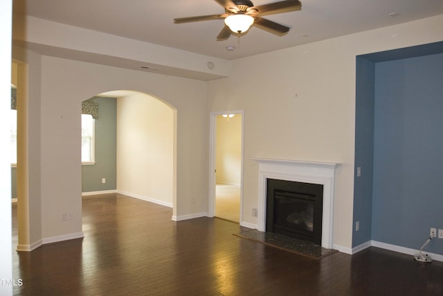 unfurnished living room with a glass covered fireplace, baseboards, arched walkways, and wood finished floors