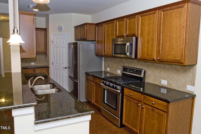 kitchen with dark wood-style floors, a sink, stainless steel appliances, pendant lighting, and backsplash