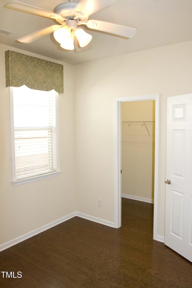 unfurnished bedroom featuring dark wood finished floors, a closet, a walk in closet, and baseboards