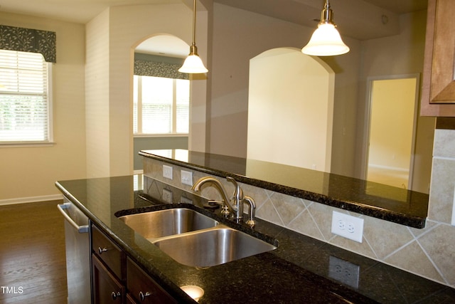 kitchen with a sink, dark stone counters, stainless steel dishwasher, and pendant lighting