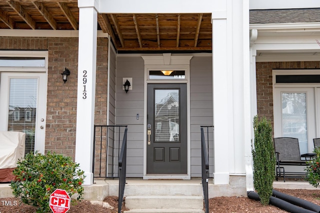 entrance to property with brick siding, a porch, and a shingled roof