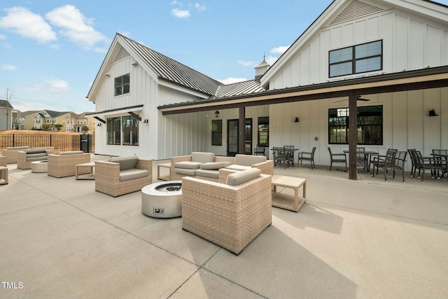 back of property with a standing seam roof, outdoor dining area, an outdoor living space with a fire pit, board and batten siding, and metal roof