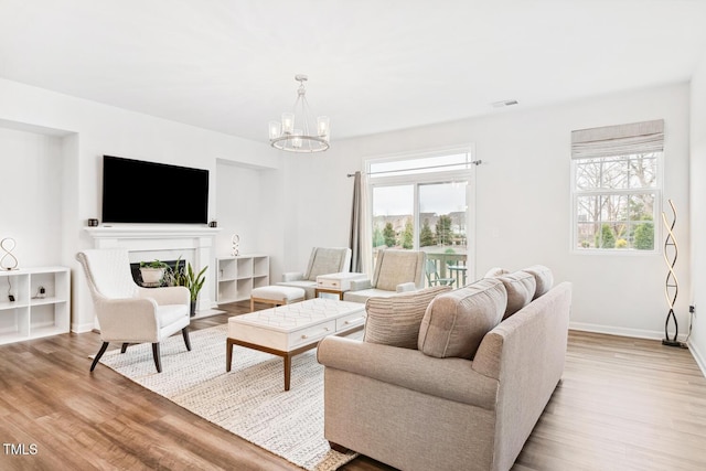 living room featuring wood finished floors, visible vents, baseboards, an inviting chandelier, and a fireplace with flush hearth