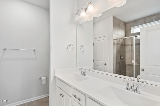 bathroom featuring a shower stall, double vanity, baseboards, and a sink