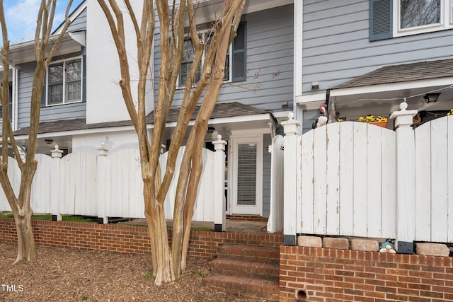 view of side of home featuring a shingled roof and fence