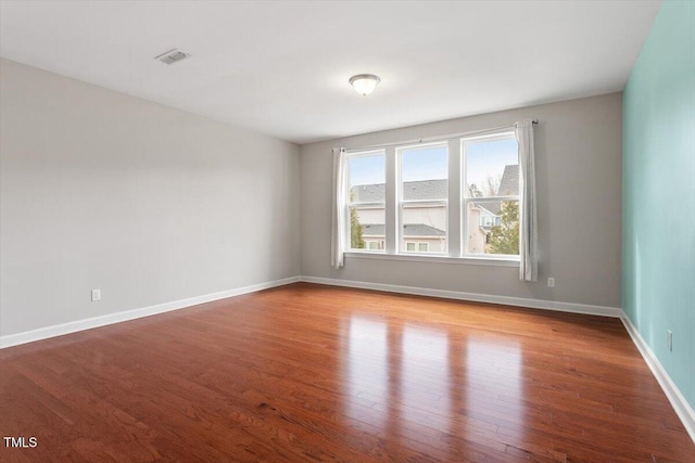 unfurnished room featuring wood finished floors, visible vents, and baseboards