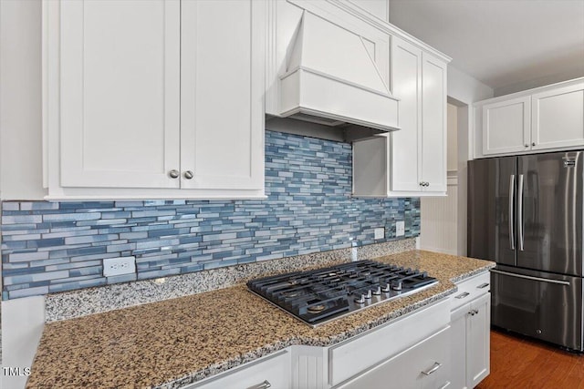 kitchen with light stone countertops, stainless steel appliances, custom range hood, white cabinets, and backsplash