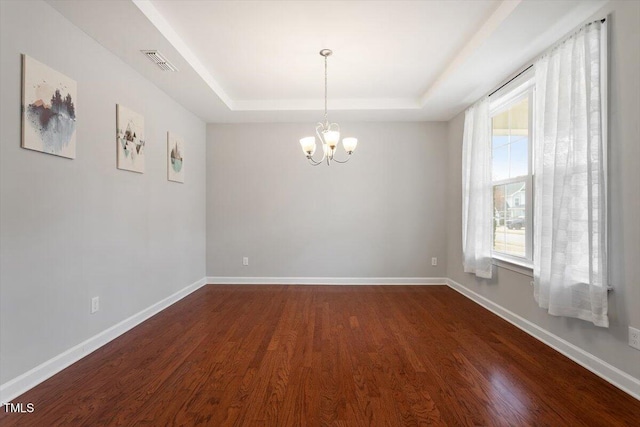 spare room featuring visible vents, a notable chandelier, dark wood finished floors, baseboards, and a raised ceiling