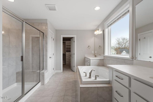 bathroom featuring tile patterned flooring, a spacious closet, two vanities, a stall shower, and a bath