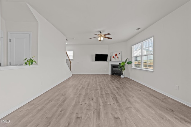 unfurnished living room featuring visible vents, baseboards, ceiling fan, wood finished floors, and a glass covered fireplace