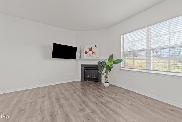 unfurnished living room featuring a glass covered fireplace, baseboards, and light wood-type flooring