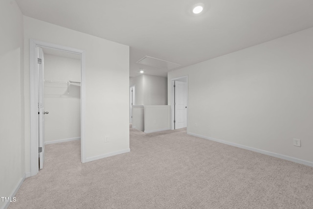 unfurnished bedroom featuring baseboards, light carpet, attic access, and a spacious closet